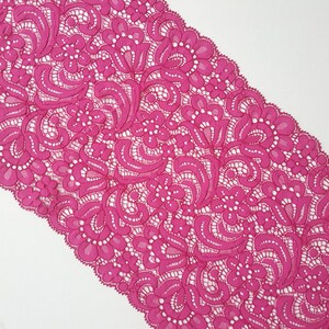 May include: Pink lace trim with a floral pattern. The lace is delicate and intricate, with a scalloped edge.