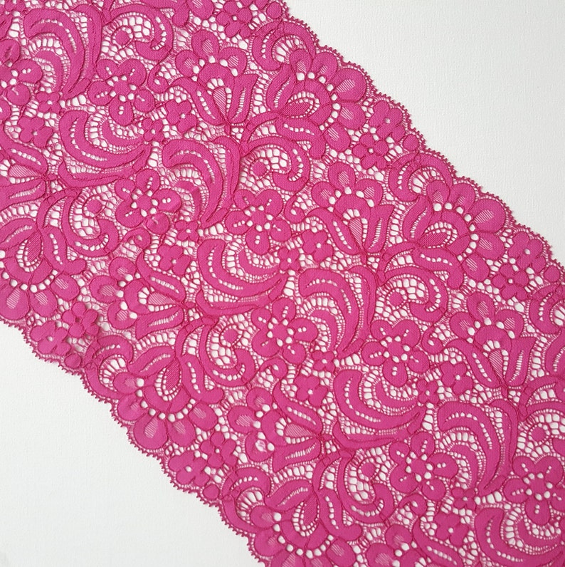 May include: Pink lace trim with a floral pattern. The lace is delicate and intricate, with a scalloped edge.
