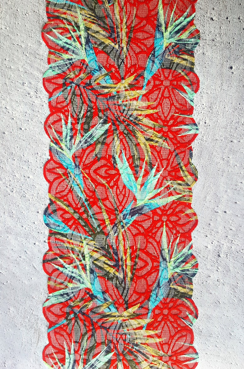 May include: Red lace trim with a floral pattern featuring blue, green, and yellow leaves. The lace has a scalloped edge.