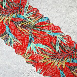 May include: Red fabric with a green, blue, and yellow floral pattern. The fabric has a scalloped edge.