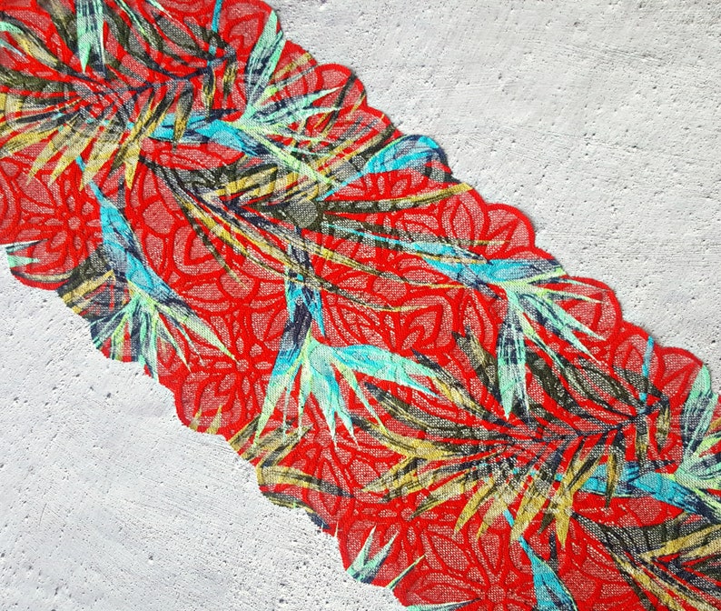 May include: Red fabric with a green, blue, and yellow floral pattern. The fabric has a scalloped edge.