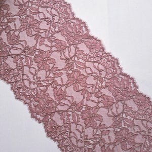 May include: Dusty rose lace fabric with a floral pattern. The lace features detailed designs of flowers and leaves, with a scalloped edge. The fabric is likely used for sewing, crafts, or apparel.