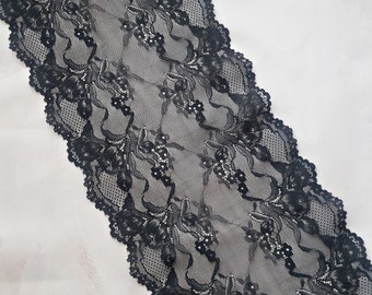 May include: Black lace trim featuring a delicate floral design. The lace is soft and has a scalloped edge.