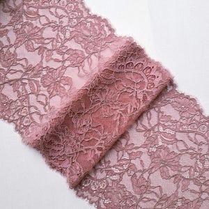May include: Dusty rose lace fabric with a floral pattern. The delicate lace is folded over, revealing the intricate design and texture. The fabric is ideal for sewing, crafting, or adding a touch of elegance to any project.