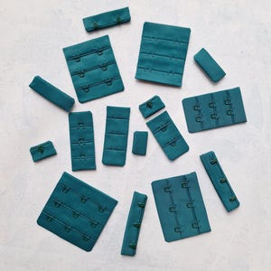 May include: Assortment of teal blue bra strap extenders with metal hooks. The extenders come in various sizes and shapes.