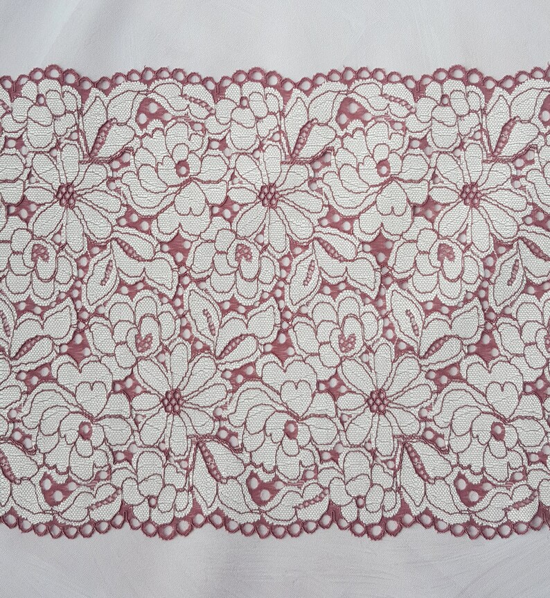 May include: A close-up of a pink lace trim with a floral pattern. The lace is delicate and intricate, with a scalloped edge.