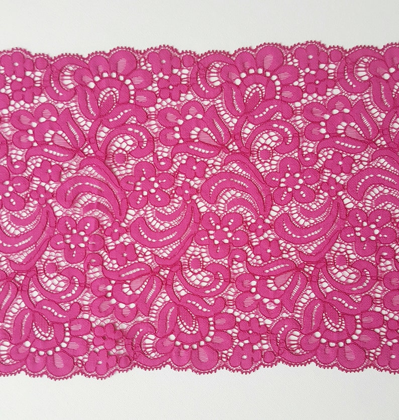 May include: Pink floral lace trim with a delicate pattern. The lace is soft and has a scalloped edge.