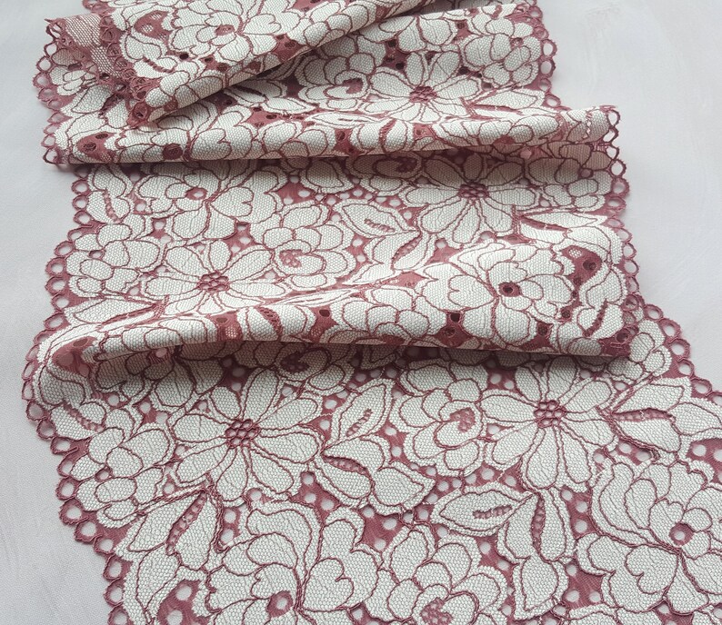 May include: Pink lace trim with a white floral pattern. The lace is delicate and has a scalloped edge.