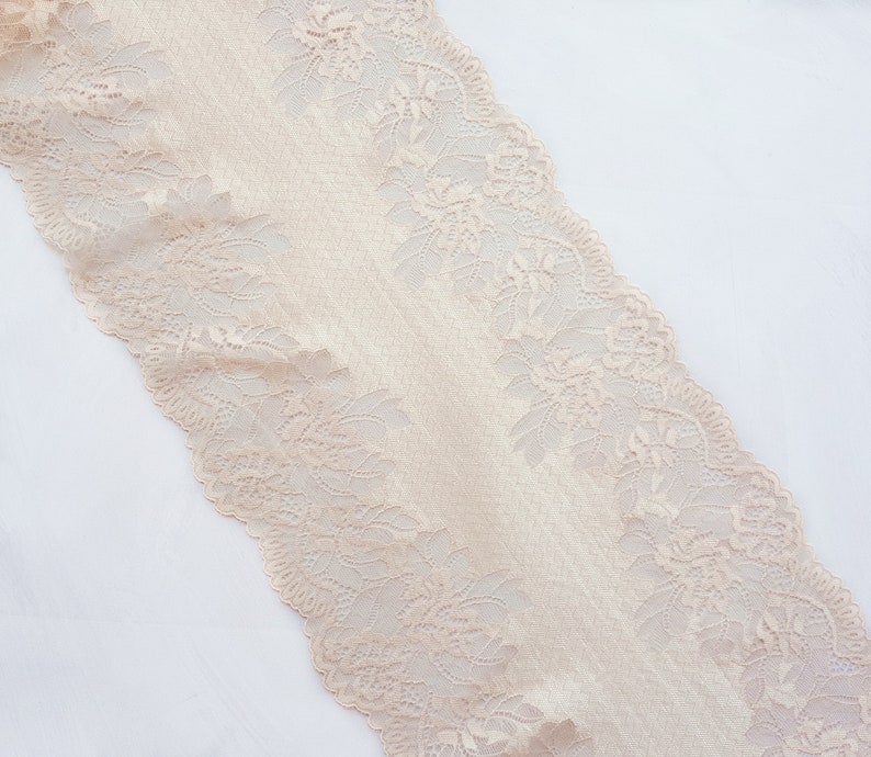May include: Beige lace trim with a delicate floral pattern. The lace is soft and has a slightly textured surface.
