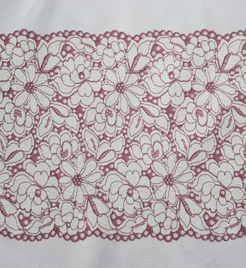 May include: A close-up of a pink lace trim with a floral pattern. The lace is delicate and intricate, with a scalloped edge.