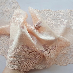 May include: Peach colored lace trim with a delicate floral pattern. The lace is soft and flowing, with a scalloped edge.