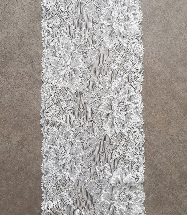 May include: White lace trim with a floral pattern. The lace is delicate and intricate, with a scalloped edge.