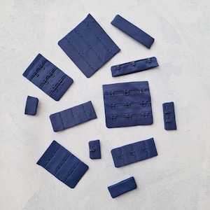 May include: Assortment of navy blue bra strap extenders with metal hooks and eyes. The extenders come in various sizes and shapes.
