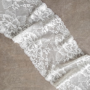 May include: White lace trim featuring a delicate floral design. The lace is soft and flowing, ideal for adding a touch of elegance to any project.
