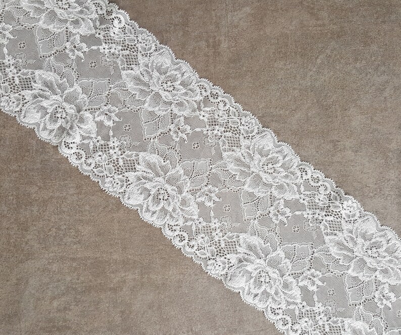 May include: White lace trim with a floral pattern. The lace is delicate and intricate, with a soft, flowing texture.