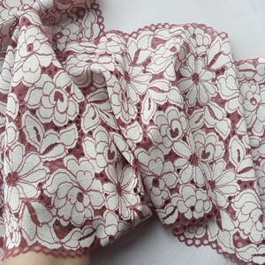 May include: A close-up of a pink and white floral lace trim. The lace has a delicate floral pattern and a scalloped edge.