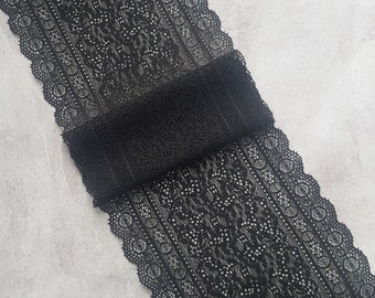 May include: Black lace fabric with a floral and geometric pattern. The lace is rolled up, displaying the intricate design and scalloped edges. Suitable for sewing and craft projects.