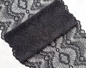 May include: Black lace trim featuring a delicate floral pattern. The lace is folded in half, revealing the intricate details of the design.