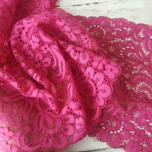 May include: Pink lace trim with a delicate floral pattern. The lace is soft and flowing, with a scalloped edge.
