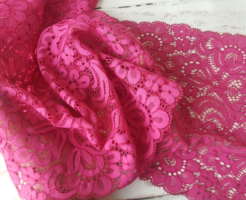 May include: Pink lace trim with a delicate floral pattern. The lace is soft and flowing, with a scalloped edge.