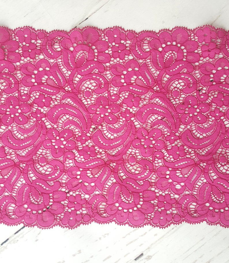 May include: Pink lace trim with a delicate floral pattern. The lace has a scalloped edge.
