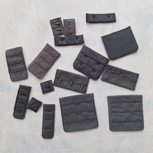 Pode incluir: Conjunto de extensões de alça de sutiã pretas com diferentes fechos de gancho e olho. As extensões são feitas de tecido e têm uma superfície macia e texturizada.