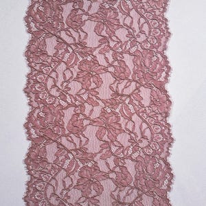 May include: Dusty rose lace fabric with a floral pattern. The lace features intricate detailing and a scalloped edge. The fabric is likely used for sewing, crafting, or adding a decorative touch to garments or home decor projects.