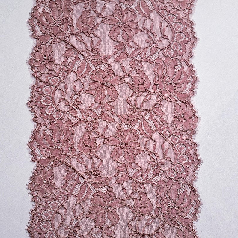 May include: Dusty rose lace fabric with a floral pattern. The lace features intricate detailing and a scalloped edge. The fabric is likely used for sewing, crafting, or adding a decorative touch to garments or home decor projects.