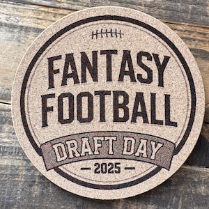 Puede incluir: Posavasos redondo con temática de fútbol americano. El posavasos presenta las palabras "FANTASY FOOTBALL DRAFT DAY - 2025" en un diseño circular con un gráfico de fútbol. El posavasos es marrón y negro.