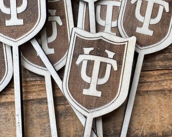 May include: A group of wooden sticks with a shield-shaped design at the top. Each shield has a white "Ψ" symbol on a brown background.