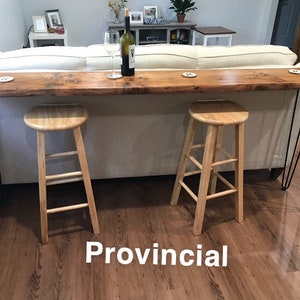 May include: A wooden console table with a live edge top and black hairpin legs. The table is placed behind a white sofa and has two wooden stools in front of it. The text "Provincial" is written on the floor in front of the table.