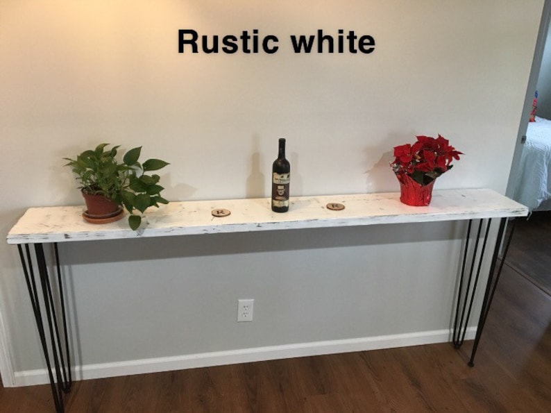 May include: White console table with black hairpin legs. The table is decorated with a bottle of wine, two potted plants, and a red poinsettia plant. The text "Rustic white" is written above the table.