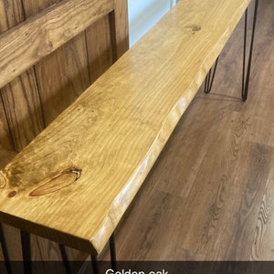 May include: A wooden console table with a live edge top and hairpin legs. The table is made of golden oak wood and has a natural finish. The table is sitting on a hardwood floor.