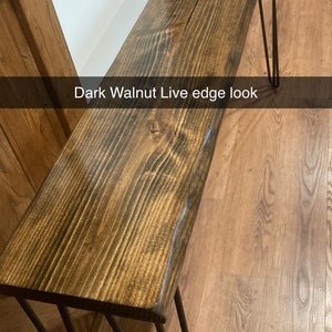 May include: A dark walnut live edge table with black hairpin legs. The table is made of wood with a natural edge and has a dark stain finish. The legs are made of metal and have a black finish.