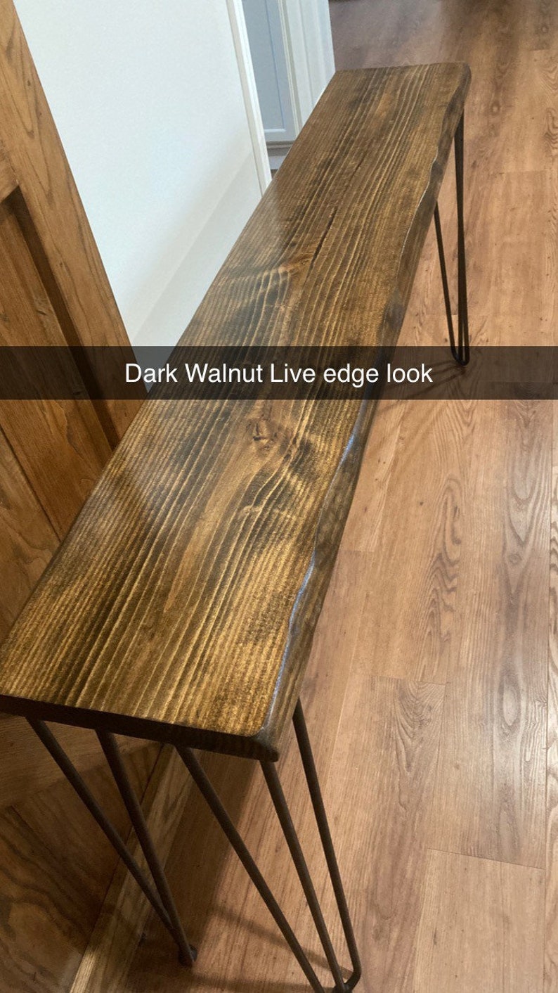 May include: A dark walnut live edge table with black hairpin legs. The table is made of wood with a natural edge and has a dark stain finish. The legs are made of metal and have a black finish.