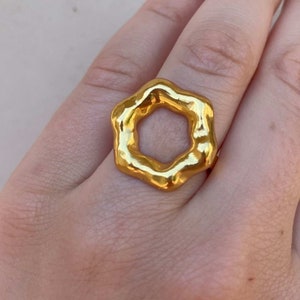 Op de afbeelding: Een ring van goudkleur met een zeshoekige vorm. De ring heeft een getextureerd, onregelmatig oppervlak.