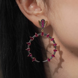 May include: A pair of crescent moon shaped earrings with a black metal frame and red gemstone accents.