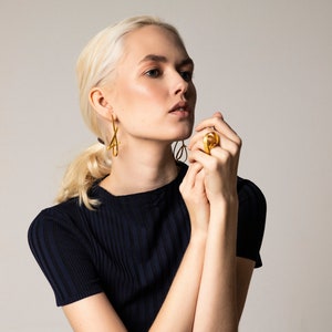 May include: A woman wearing a dark blue ribbed top with gold earrings and a gold ring on her finger.