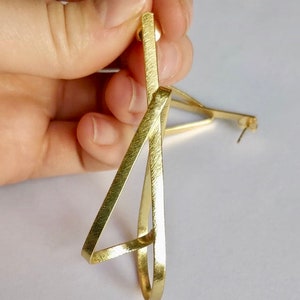 May include: Gold geometric earrings with a brushed finish. The earrings are shaped like a triangle with a circle inside.