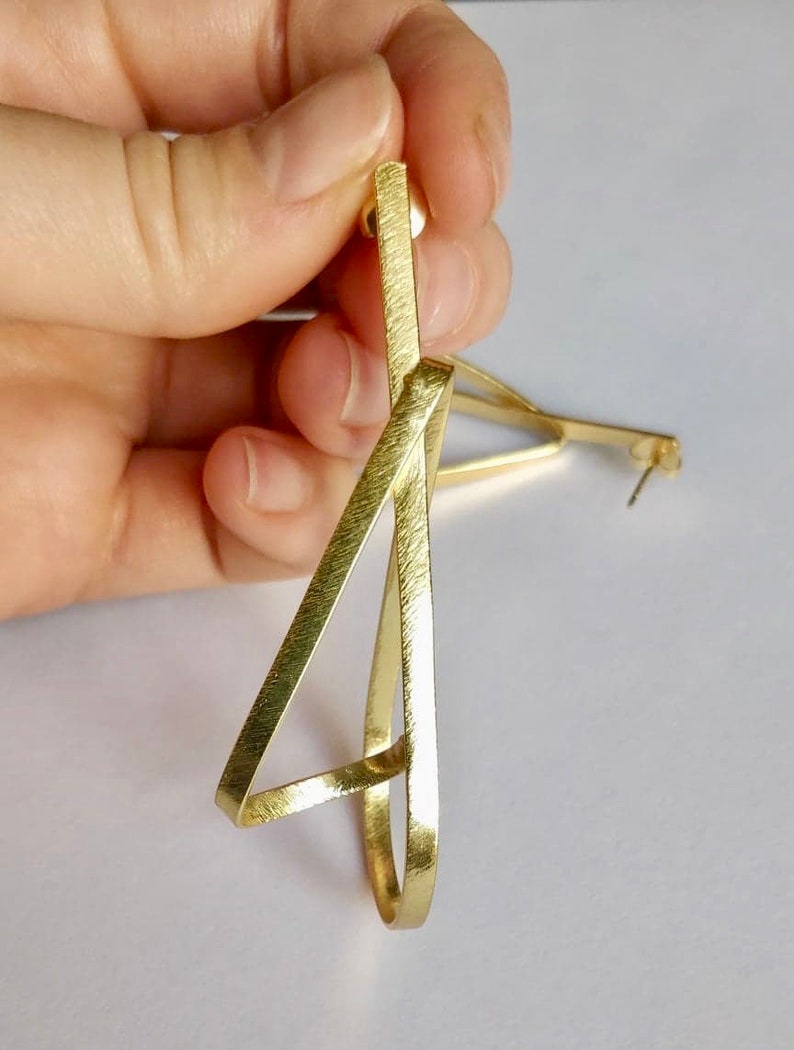 May include: Gold geometric earrings with a brushed finish. The earrings are shaped like a triangle with a circle inside.