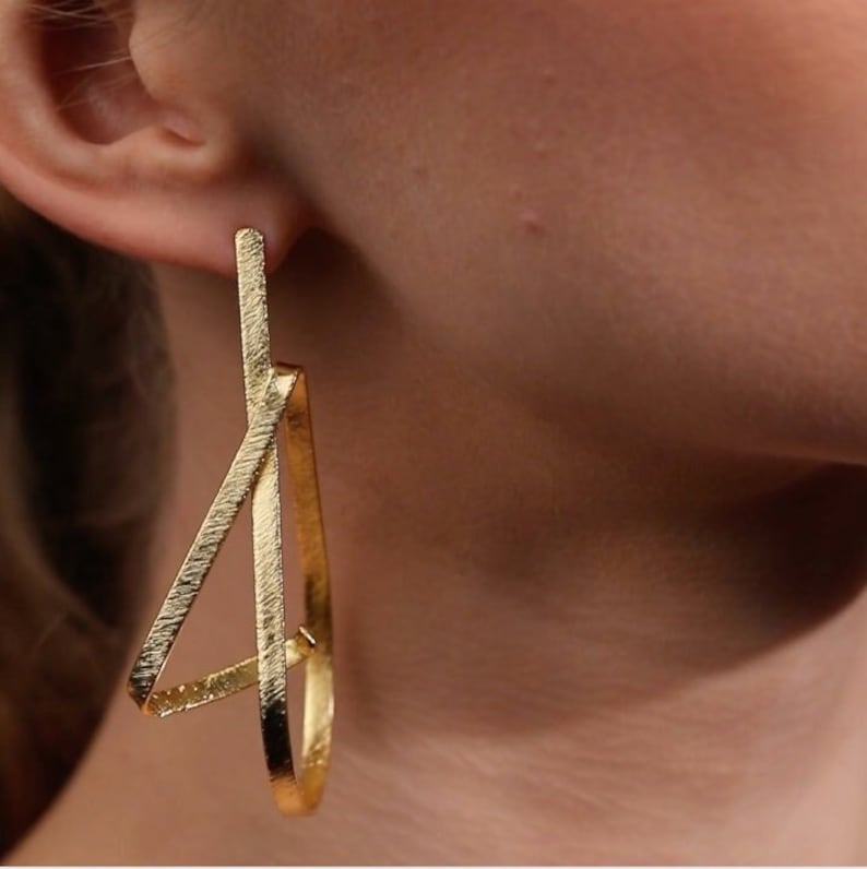 May include: Gold geometric hoop earrings with a textured finish. The earrings are in the shape of a triangle with a smaller triangle inside.