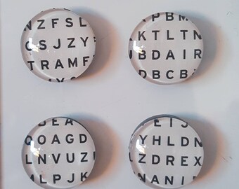 May include: Four white round magnets with black letters spelling out random words. The magnets are on a white surface.