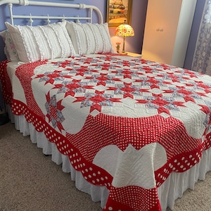 Pode incluir: Uma cama branca com uma colcha vermelha e branca e uma saia de cama de renda branca. A cama tem uma cabeceira branca com as palavras "Count Your Blessings" em uma placa acima dela. Há uma lâmpada em uma mesa de cabeceira ao lado da cama.