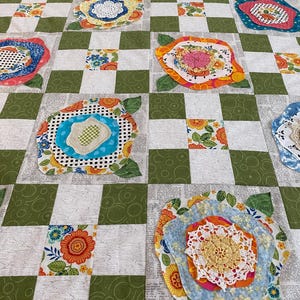 May include: A patchwork quilt with a checkered pattern in green and white. Each square features a different fabric design, including floral patterns, polka dots, and lace. The quilt is made with a variety of fabrics in shades of pink, blue, yellow, and orange.
