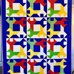 Peut inclure: Une courtepointe avec un fond bleu et un motif répétitif de formes géométriques rouges, vertes, jaunes et blanches. La courtepointe est composée de neuf carrés, chacun avec une disposition différente des formes.