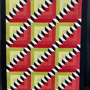 May include: A quilt with a geometric pattern of red, green, black, and white squares. The squares are arranged in a repeating pattern of overlapping squares.