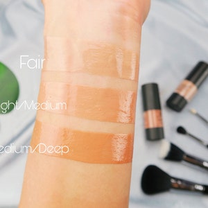 Op de afbeelding: Drie tinten foundation op de arm van een persoon, gelabeld met "Licht", "Licht/Medium" en "Medium/Donker".