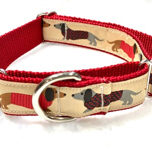 May include: Red dog collar with a beige and red dachshund print. The collar has a silver buckle and two silver D-rings.