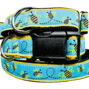 May include: A blue dog collar with a yellow trim and a black buckle. The collar is decorated with a repeating pattern of bees flying in a line.