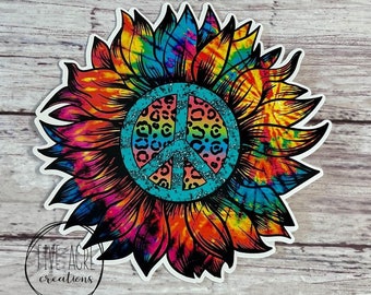 May include: A tie-dye sunflower with a peace sign in the center. The peace sign is turquoise with a glitter finish and has a leopard print design inside.